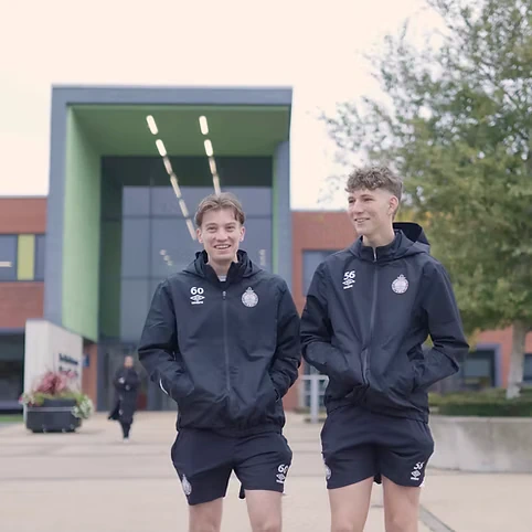 Two students talking and smiling while leaving University of Sunderland campus.